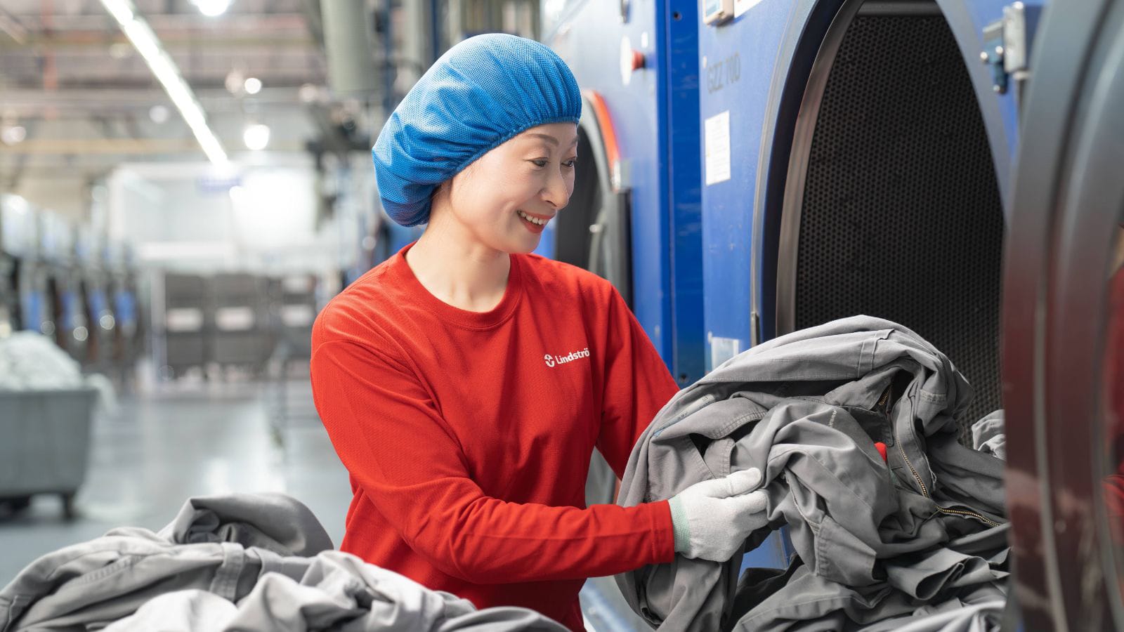 Lindström employee loading industrial workwear into a commercial washing machine.